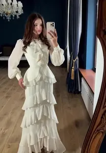 Full-length view of an elegant white tiered ruffle dress with long sleeves in a room