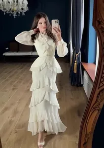 Elegant cream long-sleeved maxi dress with tiered ruffle details and waist cinch.