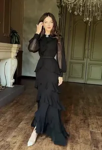 Full view of elegant black ruffled maxi dress with sheer sleeves on model in luxury interior.