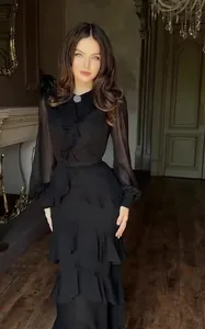 Elegant black ruffled long-sleeved maxi dress with brooch detail in a classic room