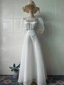 Elegante abito lungo in raso bianco con maniche a sbuffo e vita decorata con perle