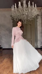 Detail van elegante jurk met lange mouwen, roze overslagtop en witte geplooide rok.