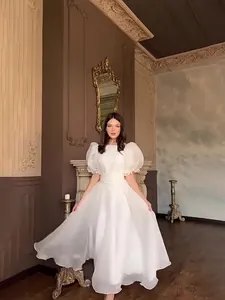 Elegante abito lungo bianco con maniche a sbuffo e dettagli decorati in interno classico.