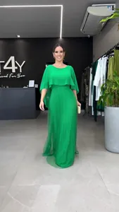 Elegante smaragdgroene maxi-jurk met cape en plooirok gedragen door een model in winkel