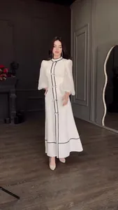Élégante robe longue blanche avec détails de nœuds noirs et manches bouffantes voilées.