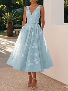Elegant light blue floral V-neck midi dress with bow-tie waist shown in a sunny garden.