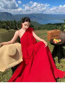 Detailed view of flowing red one-shoulder pleated maxi dress in outdoor vacation setting.