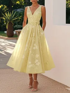 Elegant details of a yellow V-neck floral midi dress featuring a waist tie and A-line skirt.