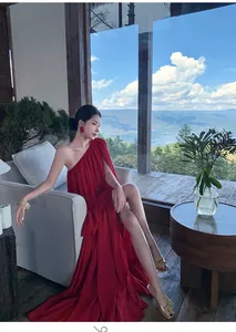Model wearing a vibrant red one-shoulder pleated maxi dress on a scenic balcony
