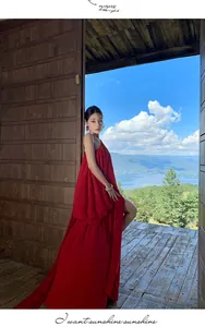 Flowing red pleated one-shoulder dress shown in a scenic outdoor balcony setting