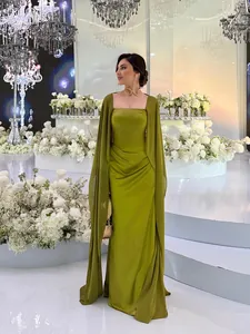 Elegante olijfgroene lange avondjurk met een modieuze cape op een prachtig wit podium.