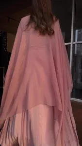 Detail van roze jurk met lange mouwen, chiffon cape en geplooide rok aan de achterkant.