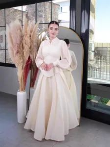 Elegant creamy white long-sleeved maxi dress with waist-cinching design in studio setting