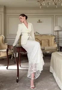 Elegante vrouw in crème blazer en witte kanten maxi-rok in een luxe kamer-setting