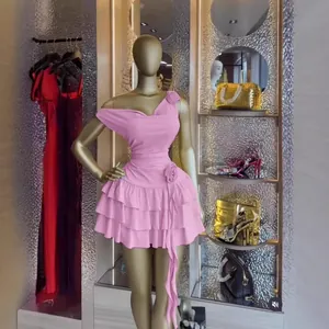 Dettaglio di un elegante abito rosa monospalla a balze con fiore 3D su manichino dorato.