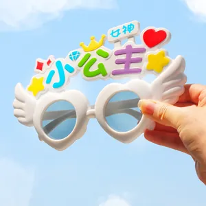 Dettaglio di divertenti occhiali da festa bianchi con lenti a cuore e ali decorative.