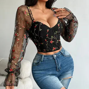 Detailed view of red floral embroidery on a black mesh corset top with long sleeves