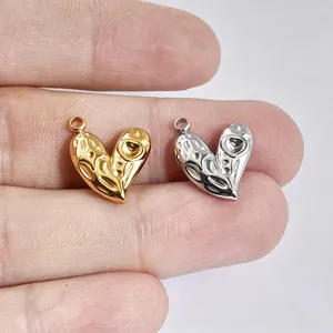 Makroansicht strukturierter Herzanhänger in Gold und Silber auf Fingern für DIY-Schmuck.