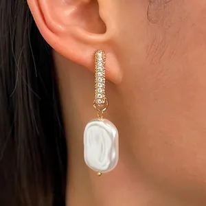 Close-up view of gold hoop earrings with pavé stones and irregular white pearl