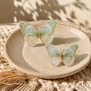 Detailed macro view of two delicate green embroidered butterfly brooches on a ceramic plate.