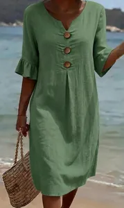 Detail of green linen dress with decorative buttons and ruffle sleeves at the beach.