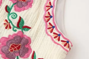Vista macro detallada del bordado floral colorido en el chaleco de tela blanca texturizada