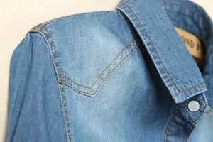 Vue détaillée du col et de l'épaule d'une chemise en jean avec des coutures contrastées fines.