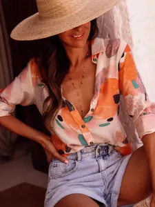 Close-up of women's orange abstract print long sleeve shirt in a sunlit resort setting