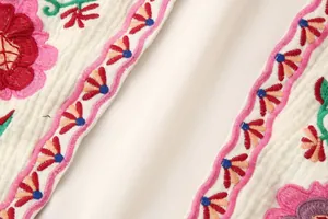 Primer plano de bordados florales vibrantes y borde decorativo en tela blanca texturizada