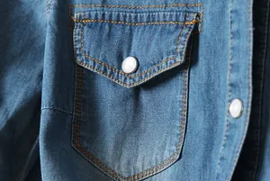 Gros plan détaillé montrant la poche et le bouton perle d'une chemise en jean bleue pour femme