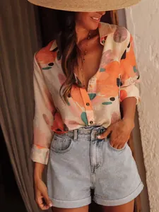 A stylish woman wearing an abstract print long sleeve shirt with blue denim shorts