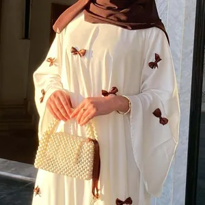Elegant detail of white dress with brown bow embellishments and a pearl beaded bag.
