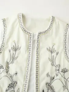 Primo piano di gilet in velluto bianco con ricamo floreale e bordi di paillettes dorate.