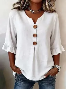 Close-up of white linen V-neck tunic with large decorative buttons and ruffle sleeves.