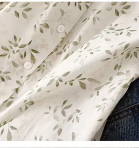 Macro detail of white floral print blouse with soft green leaves and white buttons