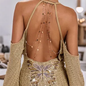 Detail van een sexy gouden top met open rug, pailletten vlinder en decoratieve kettingen.