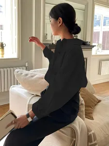 Minimalistisches schwarzes Baumwollhemd mit langen Ärmeln, getragen von einem Model im Zimmer.