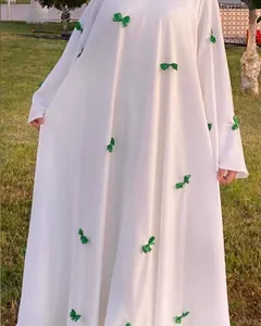 Detailed view of elegant white maxi dress featuring green bow accents and flare sleeves.