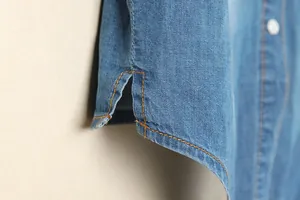 Vue détaillée de la fente latérale et des coutures contrastées d'un chemisier en jean bleu.