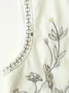 Dettaglio macro del ricamo di paillettes argento su un gilet in velluto bianco.