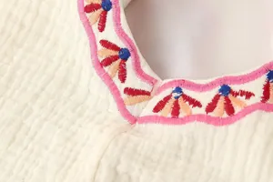Primer plano detallado del bordado floral de colores en un chaleco de gasa color crema