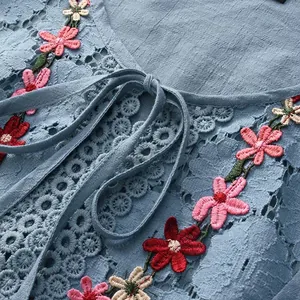 Detail van blauwe katoen-linnen top met bloemenborduurwerk en kanten strikhals