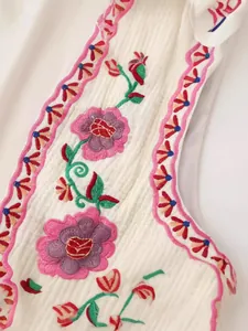 Detalle de chaleco bordado blanco con bordes rosas ondulados y motivos florales.