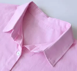 Dettaglio ravvicinato del colletto di una camicia in cotone e lino rosa con bottone bianco