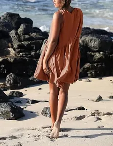 Back view of a rust orange sleeveless V-neck pleated dress on a scenic sunny beach