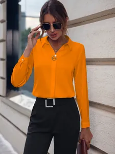 Detalle de blusa naranja brillante de manga larga con pantalones negros y cinturón cuadrado