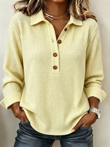 Dettaglio di una maglia a maniche lunghe da donna in tessuto nido d'ape giallo con bottoni.