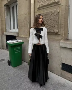 Model wearing white sequin crop jacket with large black bows in street setting