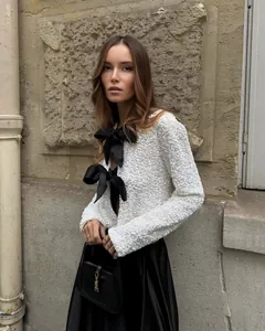Detailed view of white sequined jacket with elegant black bow tie fasteners.