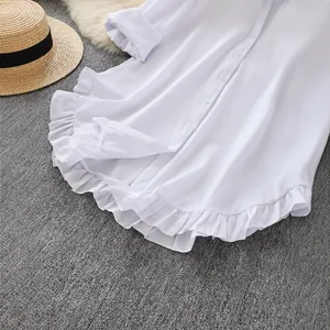 Close-up of white long sleeve shirt showing ruffled hem detail against grey rug